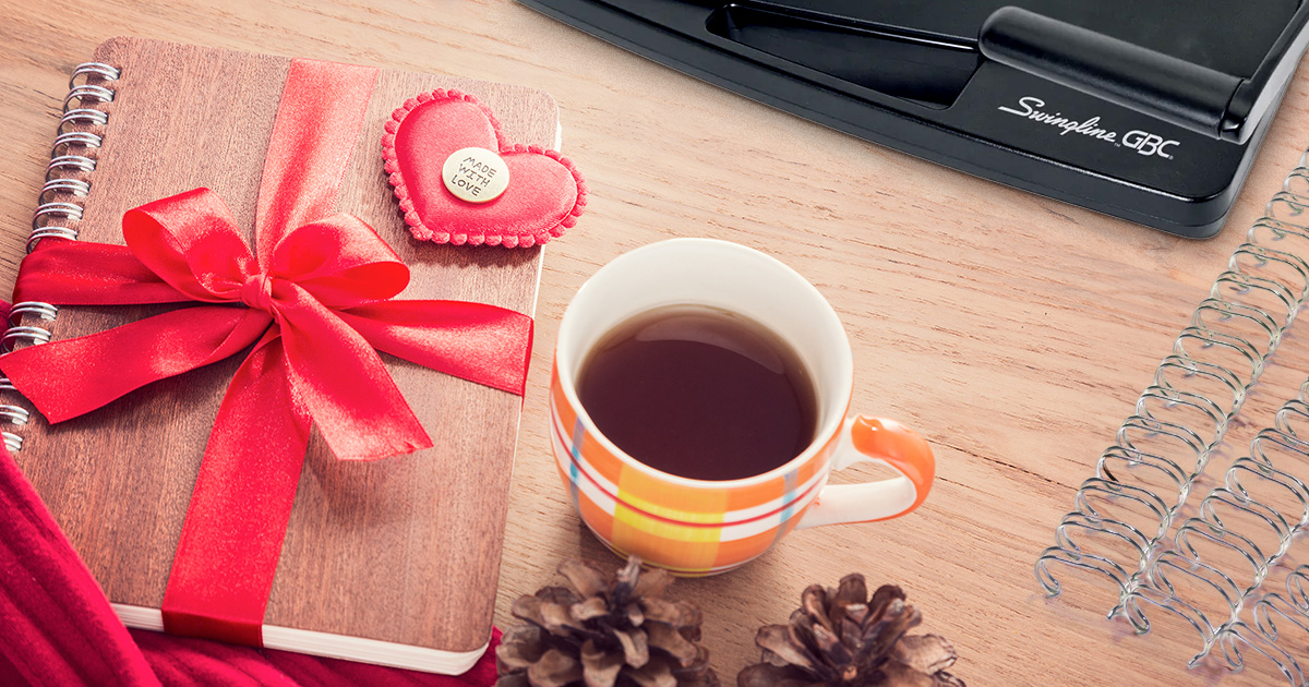 A handmade notebook positioned next to a coffee mug, with double loop wire and Swingline binding machine placed nearby.