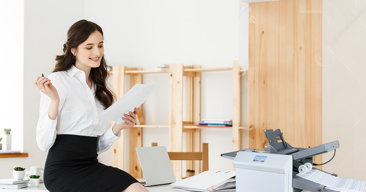 Office admin holding a piece of paper next to a paper folding machine.
