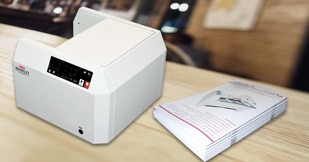 Booklet maker on a table beside a stack of finished folded booklets