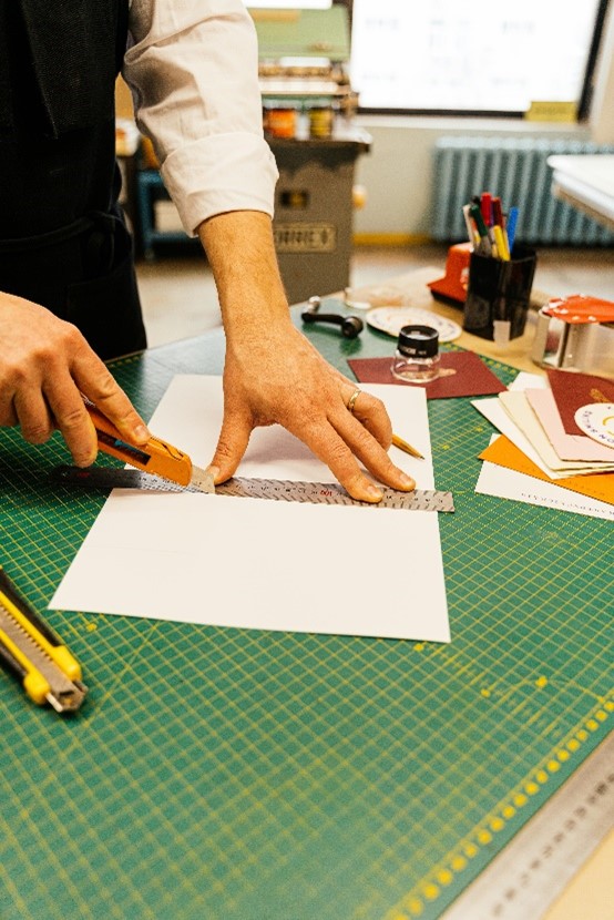 Someone cutting a piece of paper with a straight edge ruler and a craft knife